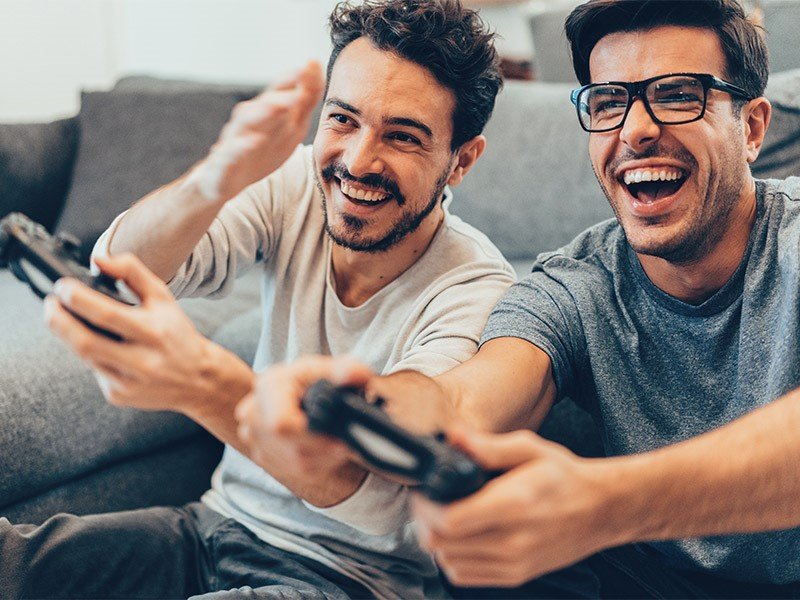 Life Extension, two smiling men on the couch with game consols in their hands playing video games